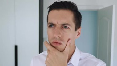 Düşünceli genç iş adamının portresi. El ele tutuşup düşünüyor, fikir üretiyor ve ofis arka planında gülüyor. Yeni fikirler aranıyor.