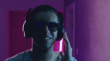Gülümseyen bir adamın portresi neon ışıkta kulaklıkla müzik dinlemekten hoşlanır. Genç erkek, mavi ve pembe neon ışıkta müzik dinliyor.