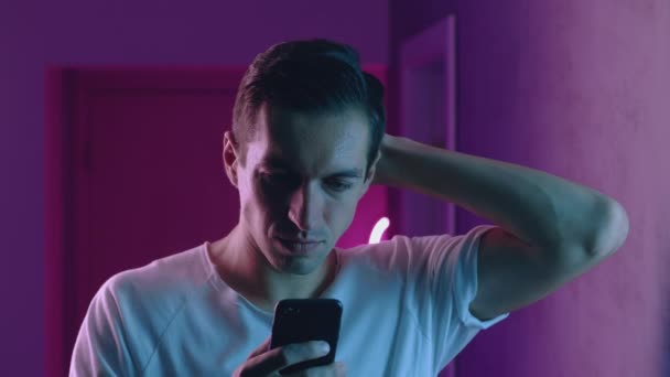 Porträt eines Mannes, der nachts sein Smartphone über Neonröhren nutzt. Junge kaukasische Männchen mit Handy-App auf blauem und rosa Neonlicht-Hintergrund — Stockvideo
