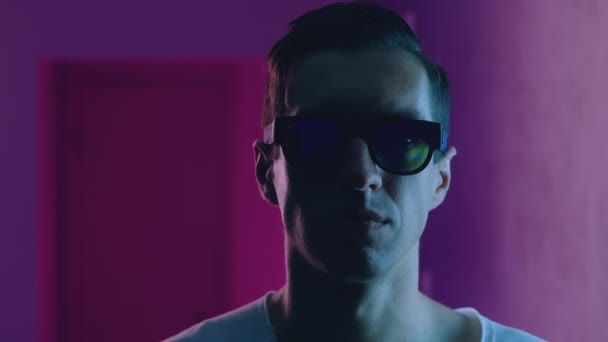 Retrato de homem hipster dentro à noite sobre luzes de néon de boate. Jovem macho em óculos de sol dentro de casa em azul e rosa neon luz fundo — Vídeo de Stock
