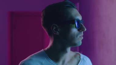 Gece kulübünün neon ışıkları altında hipster bir adamın portresi. Güneş gözlüklü genç erkek mavi ve pembe ışıklı arka planda kapalı bir yerde.