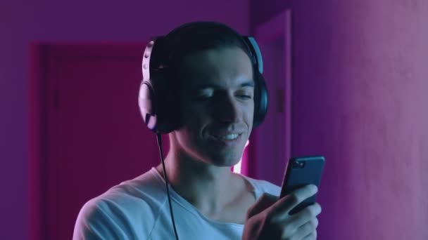 Portrait d'homme souriant aime écouter de la musique avec des écouteurs au néon. Jeune homme écoutant de la musique à l'aide de l'application smartphone sur fond bleu et rose néon — Video