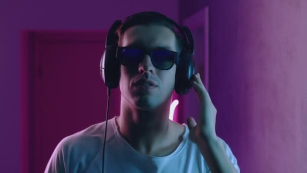 A mosolygó ember portréja szereti hallgatni a zenét fejhallgatóval neon fényben. Fiatal férfi zenét hallgat kék és rózsaszín neon fény háttér — Stock videók