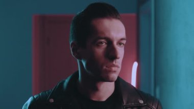 Gece kulübünün neon ışıkları altında vahşi bir adamın portresi. Ciddi erkek motorcu güneş gözlüklerini içeride mavi ve pembe ışıklı arka planda takıyor.