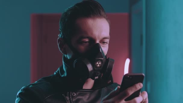 Portret van een brutale man in de beademing met behulp van een smartphone op meer dan neon lichten. Cyberpunk concept. Man in beschermende masker met behulp van mobiele app op blauwe en roze neon licht achtergrond — Stockvideo