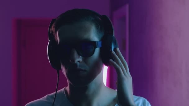 A mosolygó ember portréja szereti hallgatni a zenét fejhallgatóval neon fényben. Fiatal férfi zenét hallgat kék és rózsaszín neon fény háttér — Stock videók