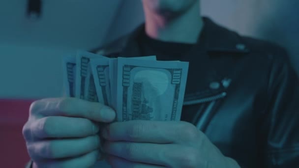 Närbild av manliga knarklangare räkna pengar mot bakgrund av neonljus i en nattklubb. — Stockvideo