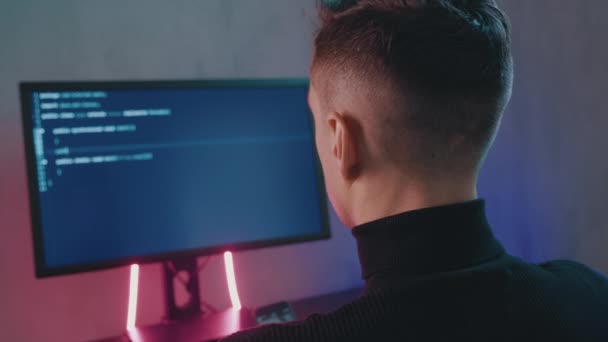 Visszapillantás az ember programozó kódoló hálózat biztonsági szoftver beltéri neon fények. Hacker gépel kódot a számítógép képernyőjén sötét irodában éjszaka — Stock videók