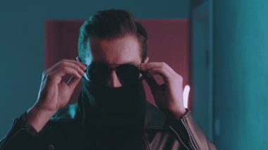 Acımasız bir adamın portresi gece kulübünün neon ışıkları altında yüzünü maske ve gözlüklerle gizliyor. Retrodalga konsepti. Güneş gözlüklü, meçhul erkek içeride mavi ve pembe ışıklı arka planda.