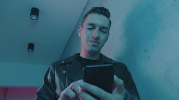 Portret mężczyzny używającego smartfona w nocy przy neonowych światłach. Młody mężczyzna kaukaski za pomocą aplikacji mobilnej na niebieskim i różowym neonowym tle — Wideo stockowe