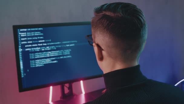 Vista posteriore del programmatore uomo codifica software di sicurezza della rete all'interno in luci al neon. Hacker digitando codice sullo schermo del computer in ufficio buio di notte — Video Stock