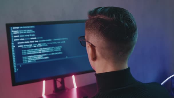 Visszapillantás az ember programozó kódoló hálózat biztonsági szoftver beltéri neon fények. Hacker gépel kódot a számítógép képernyőjén sötét irodában éjszaka — Stock videók