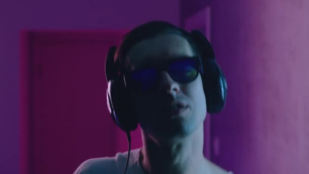 Retrato de homem sorridente gosta de ouvir música com fones de ouvido em luz de néon. Jovem do sexo masculino ouvindo música em azul e rosa neon fundo de luz — Vídeo de Stock