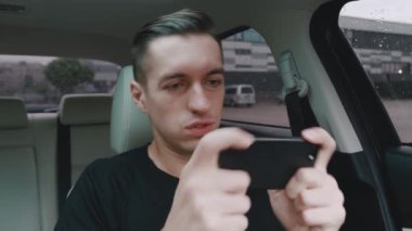 Genç adam, sürücü koltuğunda otururken akıllı telefonuyla heyecanlı bir oyun oynuyor..