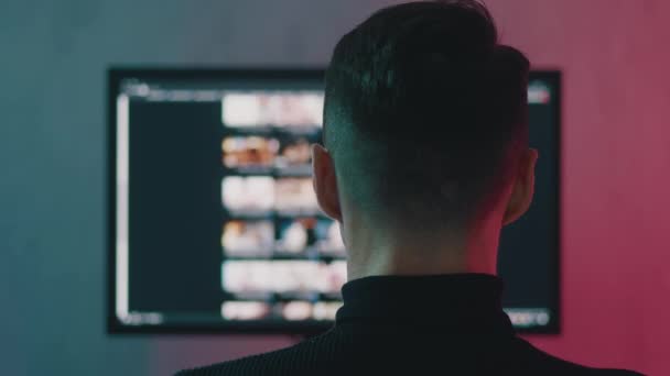 Widok z tyłu, młody człowiek oglądający porno w ciemnym pokoju w neonach. Pojęcie uzależnienia od pornografii — Wideo stockowe