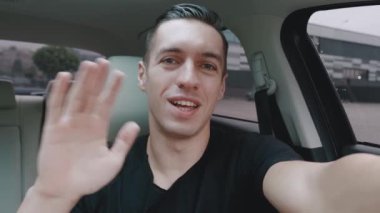 Gülümseyen genç şoför arabada otururken selfie mi çekiyor yoksa video mu çekiyor? Arabasından görüntülü konuşma yapan bir erkek gezginin portresi..