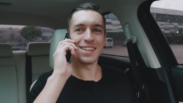 Портрет усміхненого молодого чоловіка, який розмовляє по телефону в машині. Щасливий водій спілкується за допомогою смартфона, сидячи в машині . — стокове відео