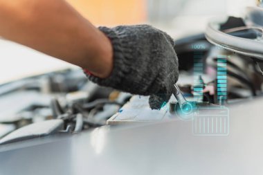 Dijital holografik ekran gösteren İngiliz anahtarıyla bir araba aküsünün üzerinde bir tamircinin eli. Modern araç bakımını ve akıllı teknolojiyi temsil eder..