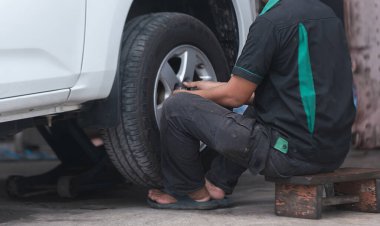 Bir tamirci kriko tarafından çalınan arabanın lastiğini değiştiriyor. Araç bakımını, oto servisini ve lastik tamirini temsil ediyor.. 