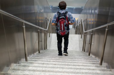 A man wearing a backpack walks down a staircase in a modern indoor setting, emphasizing travel, commuting, and everyday urban life.