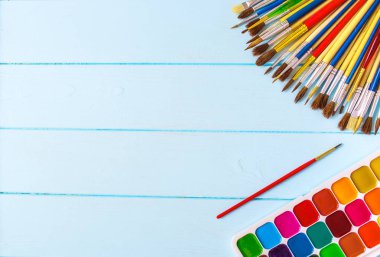 Boyalar, fırçalar ve palet mavi ahşap arka plan üzerinde. Sanatçı işyeri. Okul için banner