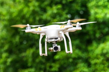 Beyaz drone ormana karşı bir havada geziniyor. Yeni teknoloji 