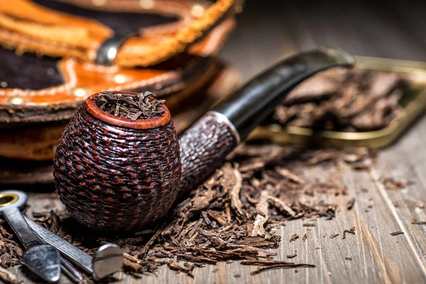 Wooden pipe with tobacco on wooden table. Tin boxes with tobacco