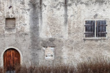 Kapalı bir kapı ve kepenkli kör pencere ile çok eski terk edilmiş bir ev bir parçası.