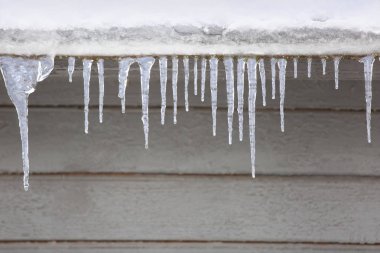 Buz sarkıtları ile ahşap bir evin çatısı