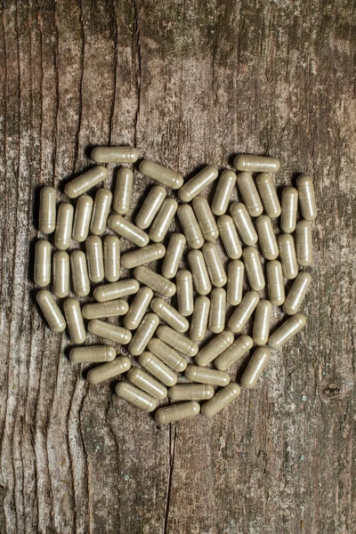 Bitkisel ilaç kapsül eski bir ahşap masa üzerinde bir kalp şeklinde koyulur.