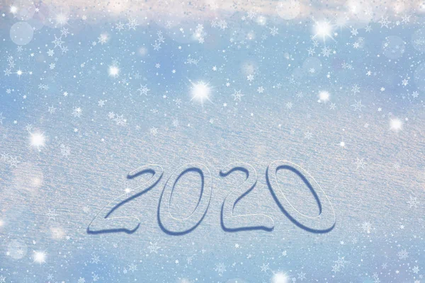 Números nevados 2020 en una superficie nevada con el telón de fondo de copos de nieve brillantes, estrellas y hermoso bokeh. Feliz fondo azul navidad . — Foto de Stock
