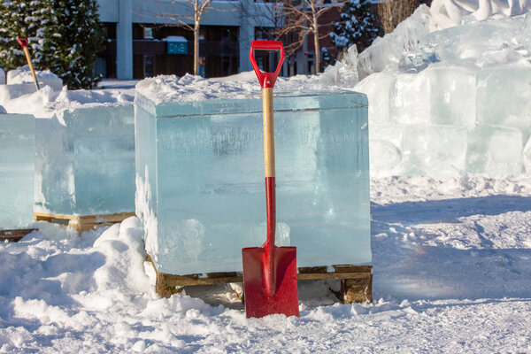 A red shovel stands near a block of pure transparent ice