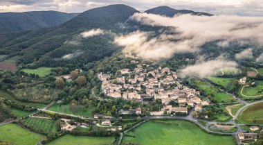 Fransa 'nın Mirmande köyünün havadan görünüşü sabah sisi ile çevrili güzel ortaçağ kasabası yemyeşil orman ve kırsal arazi yumuşak sisli gökyüzü altında tarihi mimari