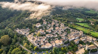 Fransa 'nın Mirmande köyünün havadan görünüşü sabah sisi ile çevrili güzel ortaçağ kasabası yemyeşil orman ve kırsal arazi yumuşak sisli gökyüzü altında tarihi mimari