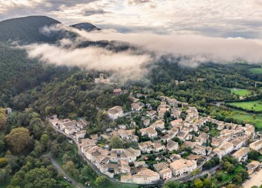 Fransa 'nın Mirmande köyünün havadan görünüşü sabah sisi ile çevrili güzel ortaçağ kasabası yemyeşil orman ve kırsal arazi yumuşak sisli gökyüzü altında tarihi mimari