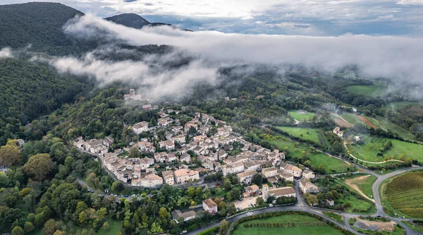 Fransa 'nın Mirmande köyünün havadan görünüşü sabah sisi ile çevrili güzel ortaçağ kasabası yemyeşil orman ve kırsal arazi yumuşak sisli gökyüzü altında tarihi mimari