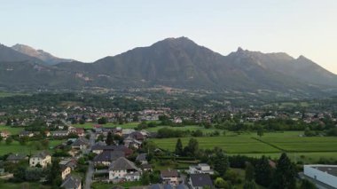 Aerial drone panorama of a French alpine city in the Savoie Alps during a bright summer morning, with warm sunlight illuminating Albertville and the surrounding mountains and valley landscape.
