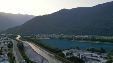 Aerial drone panorama of a French alpine city in the Savoie Alps during a bright summer morning, with warm sunlight illuminating Albertville and the surrounding mountains and valley landscape.