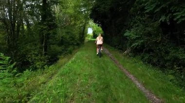 Young woman cycling on a green forest path surrounded by trees, enjoying outdoor adventure, healthy lifestyle and peaceful countryside nature