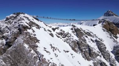 People Walking Across the Suspension Bridge on Glacier 3000 with Cable Car Station and Peak Walk in the Swiss Alps.