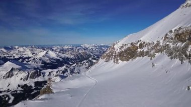 Panoramic view of the snow-covered Alpine mountains on a sunny, cloudless day, with skiers passing by on Glacier 3000 at the foot of Oldenhorn Peak.