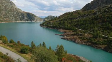 Aerial panoramic view of Emosson Dam in Finhaut, Switzerland, with turquoise lake, mountain station, parking area, and dramatic alpine scenery in the Swiss Alps.