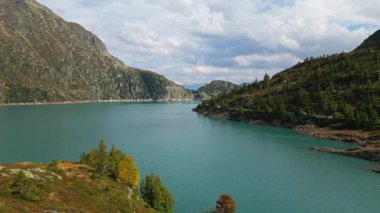 Young woman admiring scenic view of Lake Emosson in the Swiss Alps, standing on grassy hillside and enjoying peaceful alpine nature and mountain landscape.