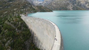 Aerial panoramic view of Emosson Dam in Finhaut, Switzerland, with turquoise lake, mountain station, parking area, and dramatic alpine scenery in the Swiss Alps.