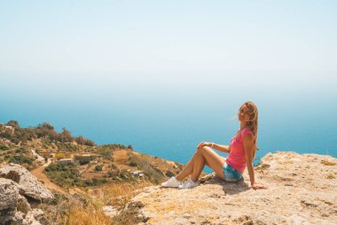 Okyanusa bakarak uçurumun kenarında oturan genç kız