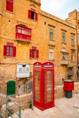 Valletta, Malta - kırmızı vintage İngiliz telefon kulübesi ve yaya köprüsü ve eski şehir Valletta sabahın erken saatlerinde geleneksel kırmızı balkon
