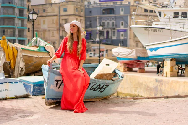 Valletta, Malta. May 20, 2018. Beautiful girl in a red dress sitting by the boats docked on the island of Malta.