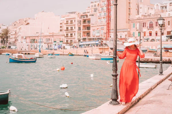 Valletta, Malta. May 20, 2018. Beautiful girl in a red dress walking by the boats docked on the island of Malta.