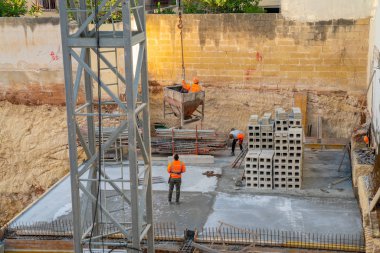 10 Mayıs 2018. Valletta, Malta. Koruyucu baretler ve vinçler tuğla ve beton kullanılarak bir ev inşa yelek giyen işçi grubu.