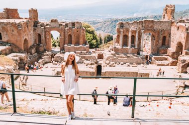 Jule 04, 2018. Taormina, İtalya. Güzel kız uzun beyaz elbise ve beyaz yaz şapka, antik Yunan tiyatro Taormina İtalya kazanı.